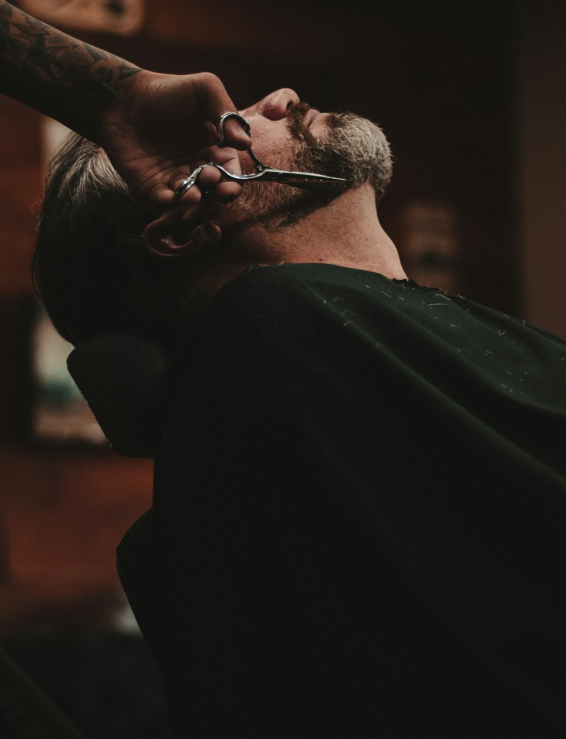 A barber working on a reclined customer, the shop dark behind them